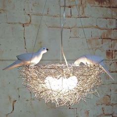 two white birds sitting on top of a bird nest hanging from a ceiling light fixture