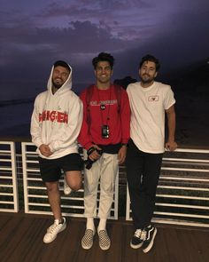 three young men posing for a photo on a deck near the ocean at night time