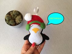 a hand holding a penguin ornament next to a potted plant with a thought bubble above it