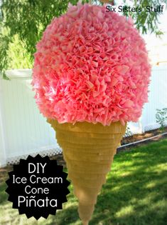 an ice cream cone filled with pink flowers in the grass next to a white fence