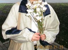 a man holding flowers in his hands while wearing a raincoat and smiling at the camera