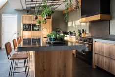 a kitchen with wooden cabinets and black counter tops, an island in the middle is surrounded by hanging potted plants