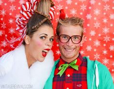 a man and woman posing for a photo in front of a christmas backdrop with snowflakes