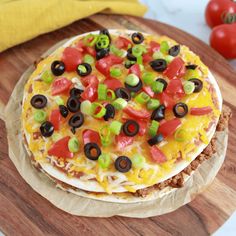 two tortillas topped with cheese, black olives and peppers on a cutting board