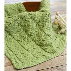 a green knitted blanket sitting on top of a wooden table next to knitting needles