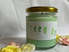 a green candle sitting on top of a table next to flowers and paper with the word green alot written on it