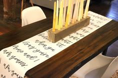 a wooden table topped with candles on top of a piece of paper next to a white chair