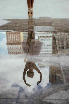 the reflection of a ballerina's feet in water with buildings reflected on it