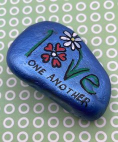 a painted rock with the words love and flowers on it sitting on a patterned surface