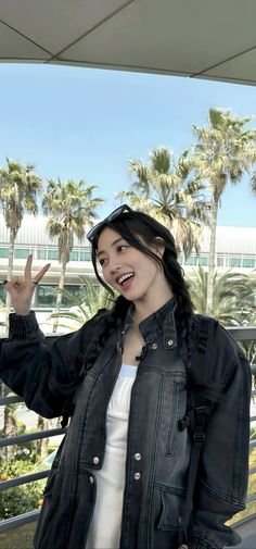 a woman in black jacket standing next to palm trees