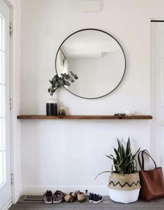 there is a mirror on the wall above a shelf with shoes and a plant in it