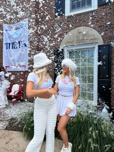 two women in white outfits standing next to each other near a building with snow falling all around them