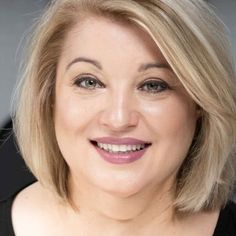 a woman with blonde hair smiling and wearing a black top on her shoulders is looking at the camera