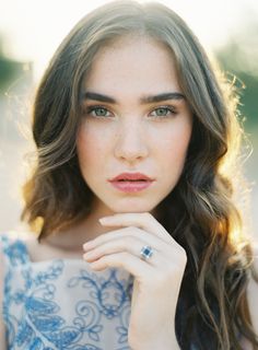 a woman with long hair wearing a blue dress and holding her hand to her face