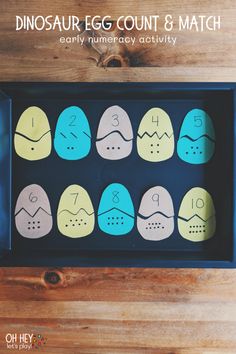 the dinosaur egg count and match game is shown in a blue box on a wooden table