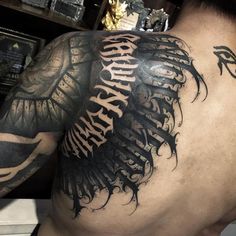 the back of a man's upper half with tattoos on his arm and shoulder