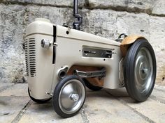 an old fashioned toy tractor sitting on top of a stone floor next to a brick wall