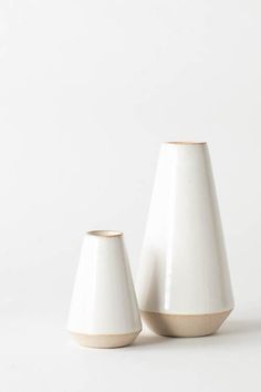 two white vases sitting next to each other on a white surface with no one around them