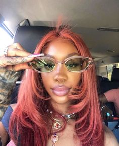 a woman with pink hair and glasses in the back seat of a car holding up her sunglasses