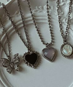 four different necklaces on a plate with a butterfly and heart charm in the middle