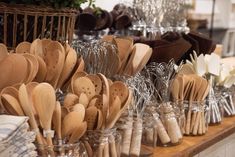 many wooden spoons are lined up on a table with glass jars filled with wood utensils