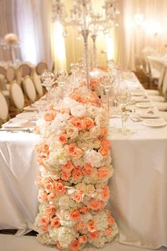 an elegant table setting with white and orange flowers on the centerpiece, chandelier and candles in the background