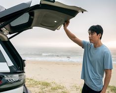 a man is holding the hood up to his car at the beach while it's open