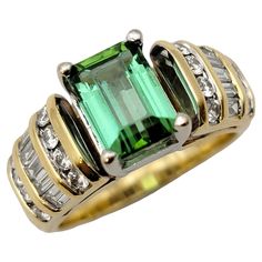 Ring size: 6.25 This pretty two tone band ring has bold color, significant sparkle and a unique design. The elegant bluish green tourmaline stone pops at the center while the sparkling diamonds shine against the warm yellow gold setting. This beautiful ring features a single 1.87 carat emerald cut green tourmaline stone, 4 prong set in polished 18 karat white gold. Flanking the bright blueish-green stone are round and baguette cut natural diamonds, separated by ridged yellow gold stations on a t Blueish Green, Warm Yellow, Tourmaline Stone, Yellow Gold Setting, Bluish Green, Channel Set, Baguette Cut, Green Tourmaline, Green Stone