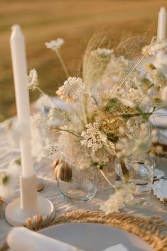 the table is set with white flowers and glass vases, candlesticks and plates