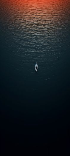 a small boat floating on top of a body of water under a red and orange sky