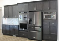 a large kitchen with gray cabinets and stainless steel appliances in the center, along with hardwood flooring