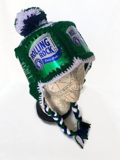 The Rolling Rock Beer hat makes a great gift for beer lovers! Love Rolling Rock beer?  Show off your love with this crocheted hat using upcycled Rolling Rock beer cans.  This ski-style hat uses six Rolling Rock beer can labels around the head (all cans were thoroughly cleaned before reuse).  The green, white and navy blue yarn used on this hat is 100% acrylic.  It has cute ear flaps with braids and a Pom Pom on top!! It fits an adult-sized head and averages 22" around. The beer cans measure 4 1/ Rolling Rock Beer, Beer Can Hat, Beer Hat, Hat With Ear Flaps, Ski Style, Rock Hat, Custom Made Hats, Ski Hat, Crocheted Hat