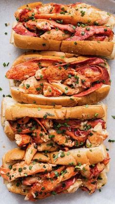 three lobster sandwiches are lined up on a tray