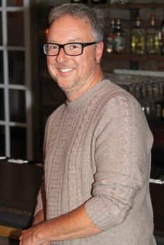 a man with glasses standing in front of a bar