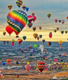 many colorful hot air balloons flying in the sky over a cityscape with buildings