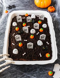 a halloween cake decorated with tombstones and pumpkins in a white dish on a table