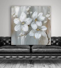 a black couch sitting in front of a painting on the wall with white flowers painted on it