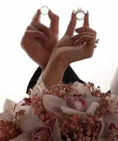 two hands holding wedding rings in front of the camera with pink flowers on it and white background