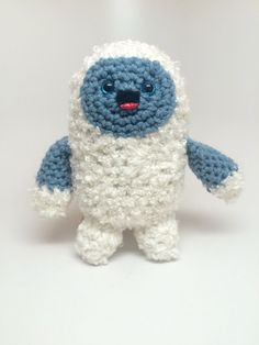 a crocheted blue and white stuffed animal on a white surface with one eye open