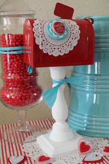 a red mailbox sitting on top of a table next to a blue vase filled with candy