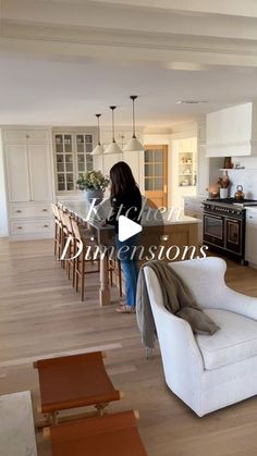 a woman standing in a kitchen next to a living room with white furniture and wooden floors