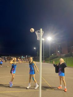 two girls are playing basketball on an outdoor court at night with the lights turned on