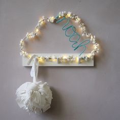 a light up sign that says welcome hanging on the wall next to a pom pom