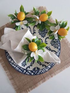 two oranges are sitting on top of a plate with white flowers and green leaves