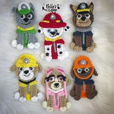 six crocheted dogs with hats and scarves are arranged in a circle on a white fur surface