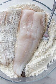 two fish fillets in a glass bowl with flour on the side and a spoon