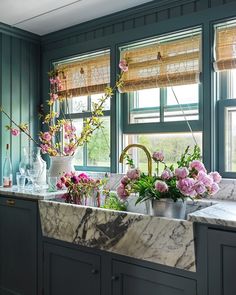 a kitchen with green walls and marble counter tops, flowers in vases on the sink