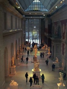 many people are walking around in a museum with statues on the walls and windows above them