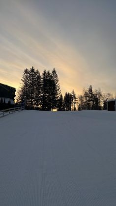 the sun is setting behind some trees on top of a snow covered hill in front of a barn