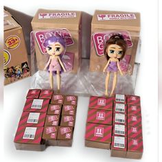 two little dolls are sitting in front of boxes with tags on them and one doll is wearing a purple dress